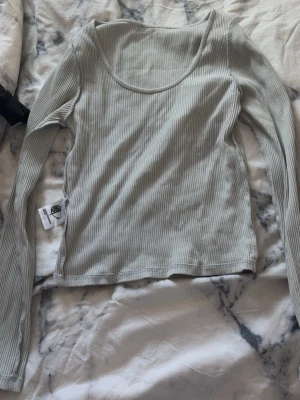Ljusgrå grön ribbad långärmad topp - Säljer en ljusgrå ribbad långärmad topp från Monki. Toppen har en rund halsringning och är tillverkad i mjuk bomullsmix. Perfekt att styla med jeans eller kjol för en enkel och snygg look.