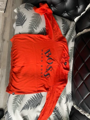 Orange långärmad tröja Hugo Boss - Cool orange långärmad tröja från Hugo Boss med stort svart BOSS-tryck på bröstet och HUGO BOSS-text under. Tröjan har rund hals och är gjord i mjukt material som känns skönt mot huden. Perfekt för dig som vill sticka ut med färg.