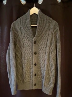 Stickad kofta - Tjenare! Säljer en snygg grå kofta med krage och kabelstickat mönster framtill. Koftan har stora svarta knappar och ribbade muddar. Perfekt för lager-på-lager och ger en chill look. Materialet är tjockt och mjukt, vilket gör den extra bekväm. Perfekt för dig som gillar den lite nyare stilen eller bara vill ha en snygg kofta! Storlek 40 som motsvara M! Passar bra på mig som är 183,5cm lång! Skicket är mycket bra inga defekter🤩hör av dig vid minsta fråga eller fundering😁mvh premium fashion