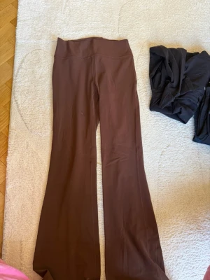 Bruna bootcut leggings från Lululemon - Säljer ett par bruna leggings från Lululemon med bootcut-ben och hög midja. Tillverkade i ett stretchigt och mjukt material som sitter skönt på kroppen. Perfekta för en avslappnad och trendig look. Storlek 8