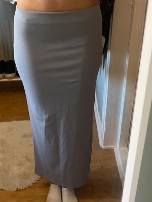 Ljusgrå långkjol i stretchigt material - Säljer en stilren ljusgrå långkjol med rak passform. Kjolen är enkel och utan mönster, tillverkad i ett mjukt och stretchigt material som sitter skönt mot kroppen. Perfekt för dig som gillar minimalistisk stil.