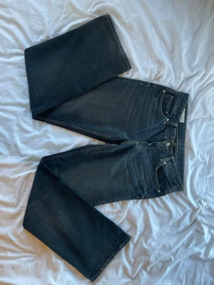 Svarta raka jeans  - Säljer ett par svarta jeans med rak passform och klassisk femficksdesign. Jeansen har diskreta slitningar och kontrastsömmar. Tillverkade i kraftig denim som ger en snygg och tidlös look.