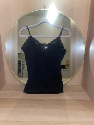 Svart spetslinnetopp - Snygg svart spetslinne med tunna axelband och vacker spetsdetalj längs v-ringad urringning i storlek s. Perfekt att styla lager på lager eller bära som den är för en chic look. Materialet känns mjukt och följsamt.skriv för fler bilder, pris kan diskuteras!💗(säljer även en exakt likadan i vit)köptes på vila💕