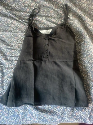 Mörk grön  linnetopp med knappar H&M - Säljer en mörk grön linnetopp från H&M med smala axelband och dekorativa knappar framtill. Toppen har en lätt rynkad struktur och är perfekt för varma dagar. Enkel och stilren design som passar till mycket.