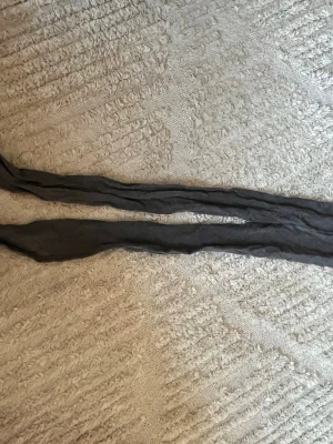 Mörkgrå tunna strumpbyxor - Säljer ett par mörkgrå tunna strumpbyxor . De är långa och har en klassisk form som passar till många olika outfits. Materialet är stretchigt och transparent, perfekt för att ge benen en snygg look.