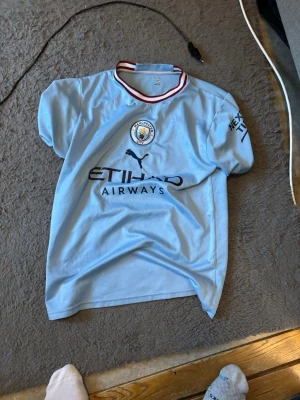 Manchester City - tröja är väldigt snygg och har en fin ljusblå färg. Den är också gjord av bra tyg som känns bekvämt och lätt att röra sig i, vilket gör den perfekt både för att spela fotboll och för att ha på sig till vardags.