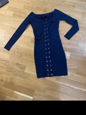 Marinblå klänning med snörning - Snygg marinblå klänning med långärmad design och cool snörning framtill. Klänningen är kort och har en kroppsnära passform som framhäver siluetten. Materialet känns mjukt och stretchigt, perfekt för dig som gillar att sticka ut. Ingen synlig logga eller märke.