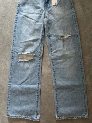 Ljusblå ripped jeans från 157 - Säljer ett par ljusblå jeans från 157 med raka ben och slitna detaljer på båda benen. Jeansen har klassisk femficksmodell, dragkedja och knapp i midjan. Perfekta för en avslappnad och trendig look.