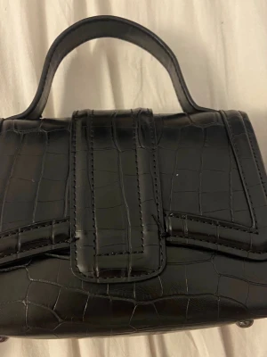 Svart croco handväska med kedja ifrån ZARA FINNS EJ LÄNGRE I HEMSIDAN  - Stilren svart handväska i croco-mönstrat konstläder med både handtag och lång kedjerem. Väskan har en markerad lockstängning och en kompakt, boxig form som ger en trendig look. Perfekt accessoar för att lyfta din outfit.