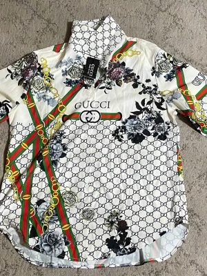 Vit blommig skjorta från Gucci - En gammal 2.5 år snygg vit skjorta från Gucci med blommigt mönster i svart och grått samt klassiska gröna och röda ränder och guldkedjor. Skjortan har tryckt logga framtill, knappar och en klassisk krage. Perfekt för dig som vill sticka ut med en exklusiv look.