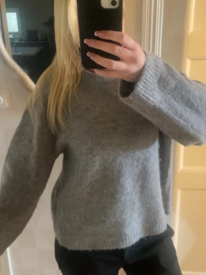 Grå stickad tröja  - Mysig grå stickad tröja med rund hals och långa ärmar. Tröjan har en avslappnad passform och ribbstickade muddar vid ärmslut och nederkant. Perfekt för lager på lager och enkel att matcha med olika outfits.