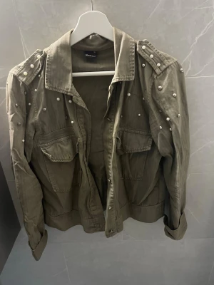 Olivgrön jacka med pärldetaljer - Stilren olivgrön jacka från Gina Tricot med dekorativa pärlor på axlar och ärmar. Storlek xs/s