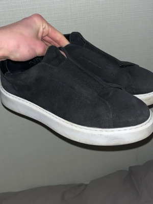 Kane skor - Säljer ett par stilrena svarta sneakers i mocka med vit, chunky sula. Skorna har elastisk resår framtill istället för snörning och detaljer i svart skinn på hälen. Perfekta för dig som gillar minimalistisk och clean stil.