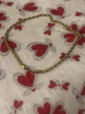 Guldfärgat tvinnat halsband - Snyggt guldfärgat halsband med tvinnad kedja som ger en cool och trendig look. Halsbandet har en klassisk karbinhake och passar perfekt till att lyfta vilken outfit som helst. Materialet ser ut att vara metall med en glansig finish.