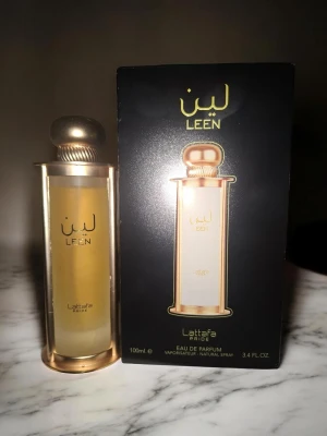 Lattafa Leen Eau de Parfum 100ml - Lattafa Leen Eau de Parfum är en lyxig parfym i en elegant, cylindrisk glasflaska med guldfärgade detaljer och rundad guldkork. Flaskan rymmer 100 ml och har en exklusiv design som verkligen sticker ut på parfymhyllan. 