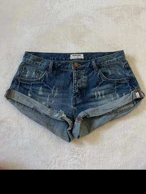 Jeansshorts OneTeaspoon - Snygga lågmidjade jeansshorts från OneTeaspoon med slitna detaljer. Klassisk femficksmodell med knapp och dragkedja framtill.   Storleken 28 motsvarar S/M, se sista bilden för måttet av midjan🥰