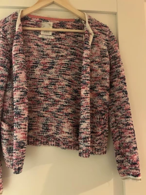 Flerfärgad stickad kofta från Gina Tricot - Säljer en stickad kofta från Gina Tricot i en mix av rosa, svart och vit. Koftan har öppen front, lång ärm och ett melerat mönster. Perfekt för lager-på-lager och ger en chill vibe till din outfit.