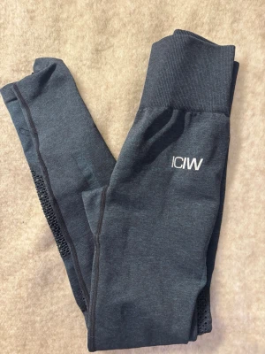 Mörkblå leggings från ICANIWILL - Supersnygga mörkgrå leggings från ICANIWILL med hög midja och bred mudd. Snygga meshdetaljer längs benen och diskret logga på låret. Perfekta för träning eller chill. Stretchigt material som sitter skönt och formar sig efter kroppen.