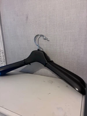 2st svarta galgar i plast - 2st svarta galgar i plast med breda axlar och metallkrok. Perfekt för att hänga upp jackor, kavajer eller andra plagg som behöver extra stöd. Enkel och stilren design som passar i de flesta garderober.