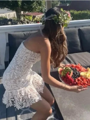 Vit spetsklänning axelbandslös - Säljer en superfin vit axelbandslös klänning med spetsdetaljer och volangkant nertill. Klänningen är kort och har en figurnära passform som framhäver siluetten. Perfekt för sommarens alla tillfällen!