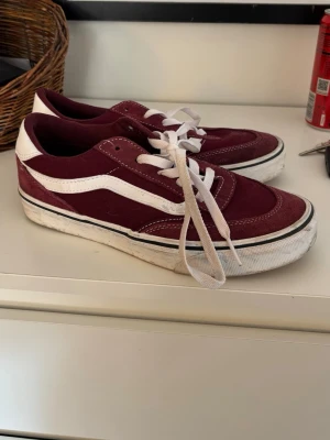 Vinröda Vans Old Skool sneakers - Säljer ett par klassiska Vans Old Skool sneakers i vinrött mocka och canvas med vita detaljer och vit sula. Skorna har den ikoniska sidostripen och vita skosnören. Perfekta för en avslappnad streetwear-look. Endast använt några gånger och köptes i sommras.