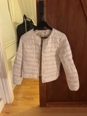 Vit dunjacka Uniqlo Ultra Light Down - Säljer en vit, superlätt dunjacka från Uniqlo Ultra Light Down. Jackan har rund halsringning, tryckknappar framtill och quiltad design. 