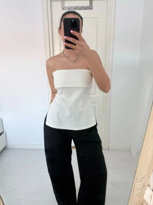 Vit axelbandslös tubtopp - Snygg vit axelbandslös tubtopp med figurnära passform och lätt utsvängd nederkant. Toppen har en stilren och minimalistisk look som passar perfekt till både jeans och kostymbyxor. Tillverkad i ett mjukt och bekvämt material.