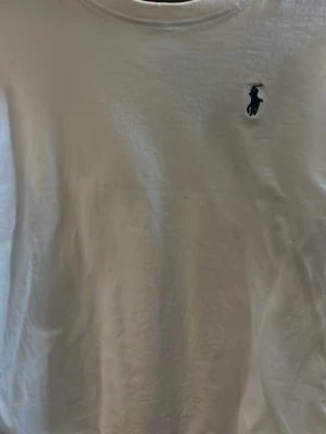 Vit t-shirt från Polo Ralph Lauren - Klassisk vit t-shirt från Polo Ralph Lauren med den ikoniska mörkblå loggan broderad på bröstet. T-shirten har rund hals och korta ärmar, tillverkad i mjuk bomull för en skön och enkel stil.