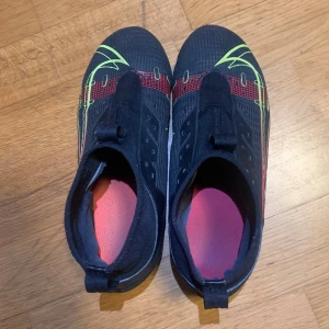 Nike mercirlal - Säljer ett par svarta  Nike mercerial med neonfärgade detaljer i gult och rött. Skorna har strumpliknande skaft och snörningsfri design för tight passform. Yttermaterialet är syntetiskt och skon har en modern, sportig look som sticker ut på planen.