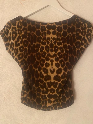 Leopardmönstrad topp med öppen rygg - Snygg leopardmönstrad topp med bred halsringning och öppen rygg. Toppen är ärmlös och har en tight passform som framhäver figuren.