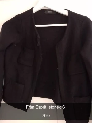 Svart kofta från Esprit - Stilren svart kofta från Esprit med rund halsringning och fyra framfickor. Koftan har en enkel, öppen design utan knappar och är tillverkad i ett mjukt material som passar perfekt till lager på lager. Långärmad modell som är lätt att matcha.