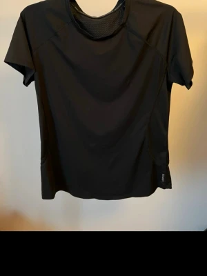 Svart tränings-tshirt från Domyos - Snygg svart tränings-tshirt från Domyos med korta ärmar och rund hals. Tillverkad i ett lätt och snabbtorkande funktionsmaterial med meshdetaljer upptill för extra ventilation. Perfekt för gymmet eller löprundan.