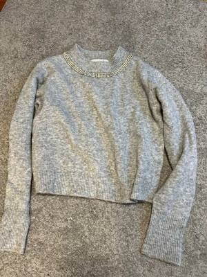 Grå stickad tröja med glitterdetaljer - Mysig grå stickad tröja med ribbade muddar och dekorerad med ”diamanter”. Bara att skriva vid frågor 