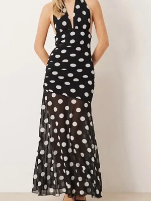Svart lång prickig klänning - Säljer en svart långklänning med stora vita prickar och djup v-ringning. Klänningen har halterneck och är ärmlös, med en transparent nederdel som ger en cool och trendig look. Perfekt för dig som vill sticka ut!