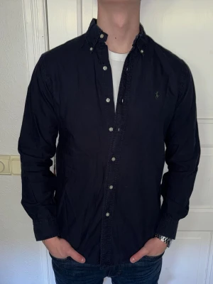 Mörkblå skjorta från Ralph Lauren - Mörkblå skjorta från Ralph Lauren i storlek S.  Fint skick till ett bra pris. Nypris: 1995kr. Mitt pris: 349kr. Vid frågor eller funderingar, tveka inte att höra av dig.