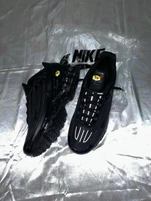 Nike Air Max Plus Tn helsvarta sneakers - Nike Air Max Plus Tn sneakers i helsvart med reflekterande detaljer på ovandelen. Skorna har en chunky sula med synlig dämpning och Tn-logga på plösen och sidan. Tillverkade i mesh och syntetmaterial för en sportig look.