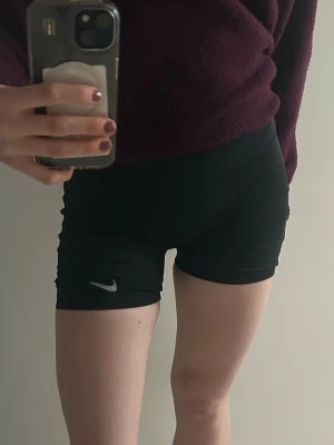 Svarta träningsshorts från Nike - Säljer ett par svarta träningsshorts från Nike med Dri-FIT material. De har en tight passform och ett diskret Nike-logga på benet. Perfekta för gymmet eller löpning och sitter riktigt skönt med hög midja.