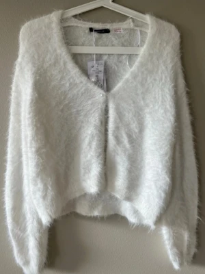Vit fluffig kofta med pärlknappar - Supersöt vit fluffig kofta med pärlknappar framtill. Koftan har lång ärm och är gjord i ett mjukt, lurvigt material som känns riktigt mysigt. Helst oanvänd med prislappen kvar.