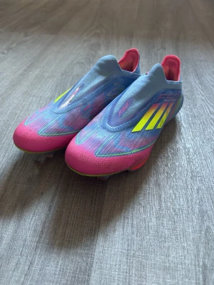 Adidas F50 blå/rosa fotbollsskor elite - Säljer ett par Adidas F50+ fotbollsskor i en riktigt snygg färgkombination av ljusblått och rosa med gula detaljer. Skorna har en strömlinjeformad design utan snörning och är tillverkade i ett lätt syntetmaterial för bästa känsla på planen. Skorna är i gott skick och är endast lite smutsiga. Påse och extra sulor medföljer. Hör av er vid minsta fundering.