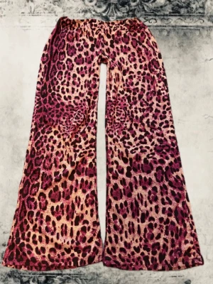 Leopardmönstrade utsvängda byxor - Snygga byxor med leopardmönster i rosa och svarta toner. Modellen har utsvängda ben och resår i midjan för skön passform. Materialet är mjukt och stretchigt, perfekt för en trendig och bekväm look. Passar mig med storlek 40/42, sydda av mig ! 