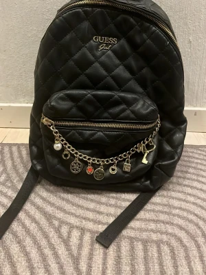 Svart quiltad ryggsäck från Guess - Snygg svart quiltad ryggsäck från Guess med guldfärgade detaljer och dragkedjor. 