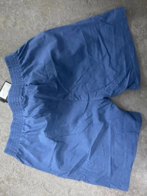 Blå bomullsshorts med resårmidja - Snygga blå shorts i bomull med elastisk midja för skön passform. Perfekta för varma dagar och enkel att matcha med t-shirt eller linne. Modellen är enkel och stilren utan extra detaljer.