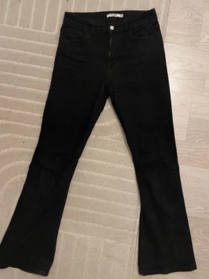 Svarta bootcut jeans från NA-KD - Säljer ett par svarta bootcut jeans från NA-KD. Jeansen har klassisk femficksmodell, hög midja och utsvängda ben. Tillverkade i ett stretchigt denimtyg för skön passform. Perfekta för dig som gillar en tidlös och trendig look.