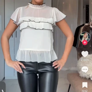 Beige volangblus från Nelly - Supersöt vit / beige blus från Nelly med volanger och svarta kanter. Inga tecken på användning då jag endast haft på mig den en gång men tycker inte jag passar i den