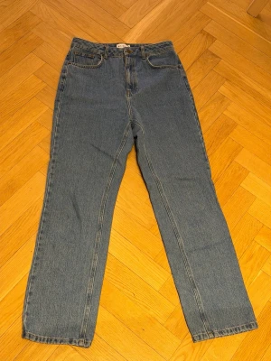 Blå raka jeans från NA-KD - Klassiska blå jeans från NA-KD med rak passform och hög midja. Jeansen har fem fickor, bälteshällor och stängs med knapp och dragkedja. Tillverkade i denim med en tidlös tvätt som passar till allt.