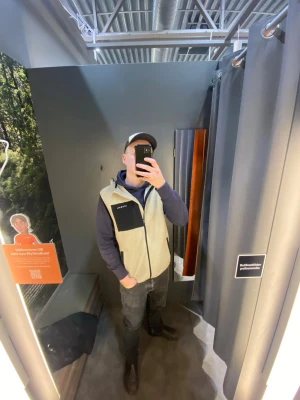 Beige dunväst från Ocean Works - Snygg beige dunväst från Ocean Works med dragkedja framtill och kontrasterande svart bröstficka. Västen har en modern passform och är tillverkad i ett mjukt, quiltat material som håller värmen. Perfekt att slänga över en hoodie för en avslappnad look.