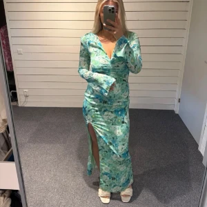 Grönblå adoore långklänning med slits - Säljer denna supersnygga långklänning i gröna och blå toner från adoore. Klänningen har v-ringning, långa ärmar och en hög slits framtill. Ordinarie pris 1595kr