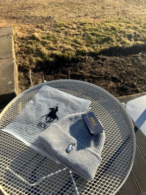 Grå mössa Polo Ralph Lauren - Snygg grå ribbstickad mössa från Polo Ralph Lauren med klassisk broderad logga framtill. Mössan har uppvikt kant och är tillverkad i mjukt material som håller dig varm. Perfekt accessoar för kyliga dagar.