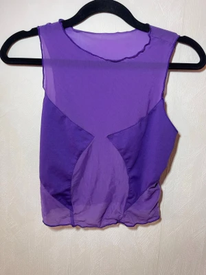 Lila mesh ärmlös topp - Snygg ärmlös topp i lila mesh med transparenta partier och rund hals. Toppen har en croppad passform och coola sömdetaljer framtill som ger en edgy vibe. Perfekt att styla med höga jeans eller kjol för en trendig look. Shein, storlek M. Helt ny, oanvänd. Djur, rök och parfymfritt hem.
