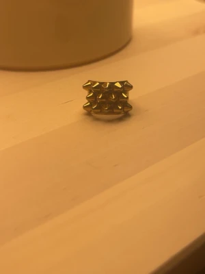 Guldig ring med nitar från Edblad - Cool ring i guldfärgad metall från Edblad med flera spetsiga nitar på ovansidan. Ringen har en chunky design som verkligen sticker ut och passar perfekt för dig som gillar statement-smycken. Märket är ingraverat på insidan av ringen.